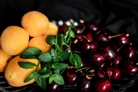 Fresh ripe cherries and apricots on a black background.の写真素材