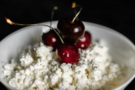Cottage cheese with cherries in a white bowl on a black backgroundの写真素材
