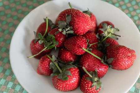 Strawberries on a white plate with green tablecloth in the backgroundの写真素材