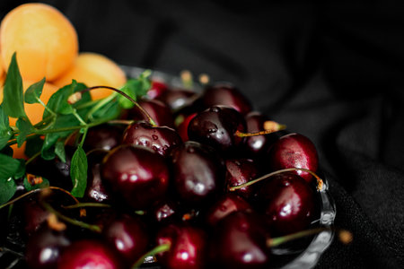 Cherries and apricots in a glass bowl on a black backgroundの写真素材