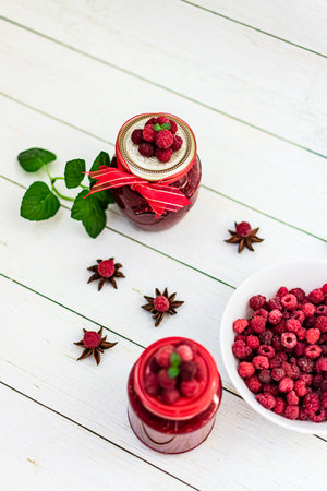 Raspberry jam in glass jar and fresh berries on white wooden backgroundの写真素材