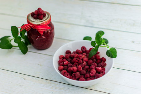 Raspberry jam in a glass jar and fresh berries on a white wooden background