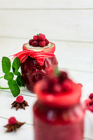 Homemade raspberry jam in glass jar with fresh raspberries on white wooden backgroundの写真素材