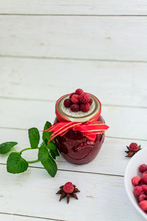 Homemade raspberry jam with fresh raspberries and mint on white wooden background