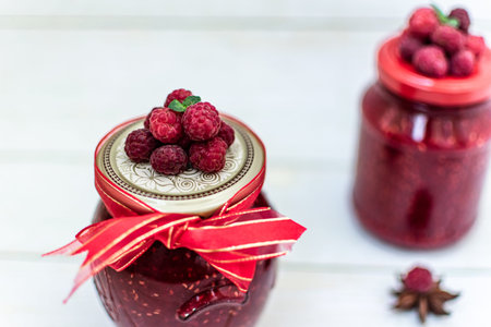 Homemade raspberry jam in a glass jar on a white wooden background