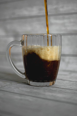 dark beer with dense foam in a glass beer mug on a light backgroundの写真素材