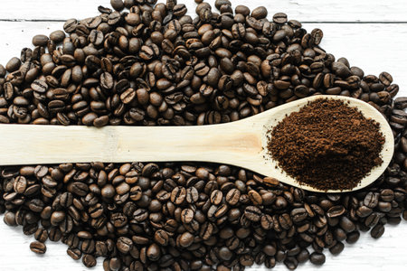Roasted coffee beans and ground coffee in wooden spoon on white wooden backgroundの写真素材