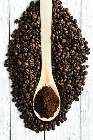Roasted coffee beans and ground coffee in wooden spoon on white backgroundの写真素材