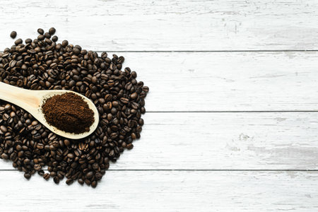 Coffee beans and ground coffee in wooden spoon on white wooden backgroundの写真素材