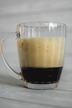 dark beer with dense foam in a glass beer mug on a light backgroundの写真素材