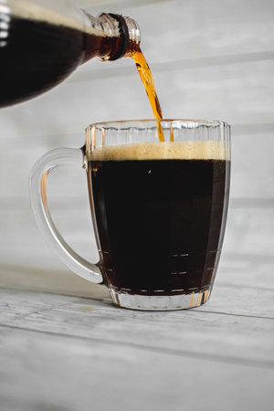 dark beer with dense foam in a glass beer mug on a light backgroundの写真素材