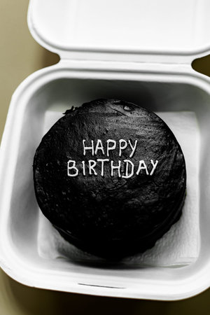 Happy Birthday black cake on a white paper box. Close up.