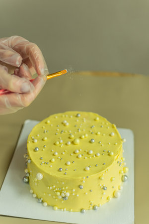 Female gloved hand decorating a yellow cake with pearls.の写真素材