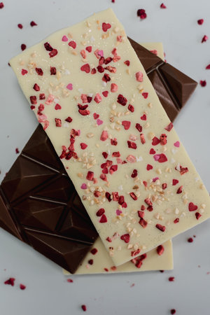 Chocolate bar with heart-shaped sprinkles and chocolate pieces on white background
