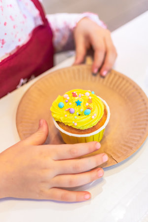 Cupcake decorated with colorful sprinkles in a children's handの写真素材