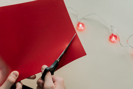 Hands of woman cutting red envelope with scissors on white background with Christmas lightsの写真素材