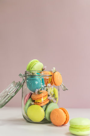 Colorful macarons in glass jar on pastel pink backgroundの写真素材