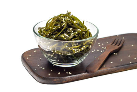 Seaweed kelp (Laminaria) in a glass bowl, sprinkle sesame seeds on a wooden board, Isolate on white background. Seaweed salad. Healthy food concept.の写真素材