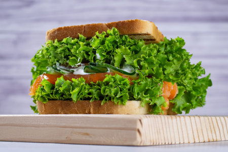 Sandwich with fresh salmon, lettuce, cucumber and sauce on a light colored cutting board, on a light background. Homemade. Healthy convenience food.の写真素材