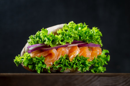Sandwich with fresh salmon, red onion and lettuce in a flavorful pita, on a cutting board on a dark background. Home cooking. Healthy fast food.の写真素材
