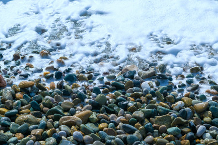 Sea pebbles and sea foam. Rocky seashore. Natural backgrounds and textures. Small stones and a wave...