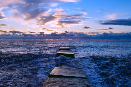 Beautiful sunset over the sea. Waves crash on the pier. Seascape. Marine background. Postcard, wallpaper.の写真素材