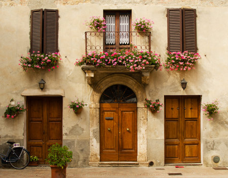 Facade of old house in Pienza with windows,  balcony with flowers,  wooden doors, plants. Tuscany, Italyの写真素材