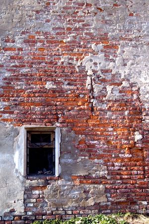 Red brick wall with close window and pieces of plaster.の写真素材