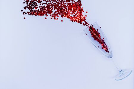 Heart-shaped vibrant red confetti poured out of champagne glass on white background with copy space for text. Top view and flat lay. Holiday, love and celebration concept. Concept for valentines day.の写真素材