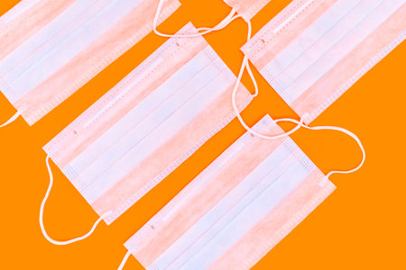 Background of medical masks on an orange backdrop. Concept of protection against flu, viruses and...