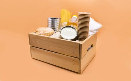 Wooden donation box with food: canned food, pasta, peas, millet, sugar, vegetable oil, cookies on an orange background.の写真素材