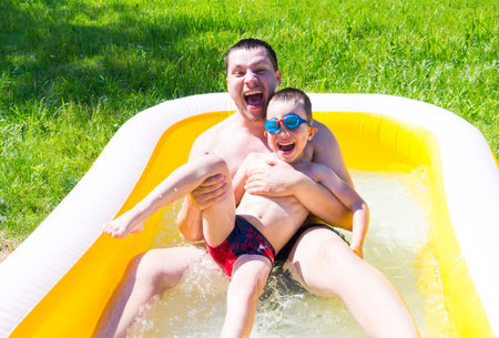 Dad plays with his son in the inflatable pool. Child with father are having fun, splashing, laughing...