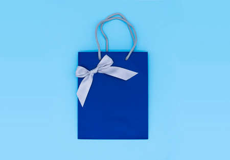 A blue gift bag with a silver ribbon on blue background. Top view, copy space. Gift concept. New year, Womans day. Valentines day. Ready for birthday party.の写真素材