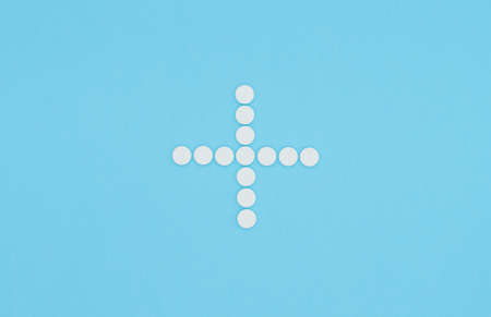 Medical cross lined with white pills. Top view on blue background. Flat layの写真素材