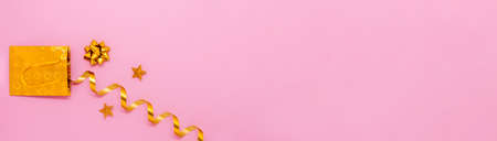 Festive banner with golden gift bag with ribbon and stars on pink background. Flat lay, top view. Copy space for your text.の写真素材