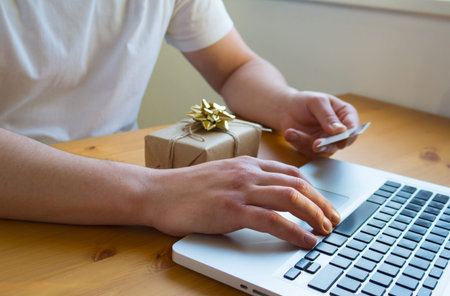 A man orders and pays for gifts on the Internet on a laptop without leaving home with a credit card....
