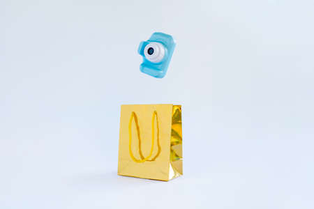 Golden gift bag with a blue camera falling into it from above on a white background. The concept of a gift of electronics and photographic equipment for the holiday, gift shopping.の写真素材
