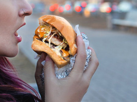 Hungry girl eating a big burger take away on the street close upの写真素材