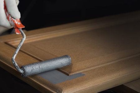 Person remonier paints a wooden product, kitchen facade with a roller with gray paint or primer. Close up photo copy spaceの写真素材