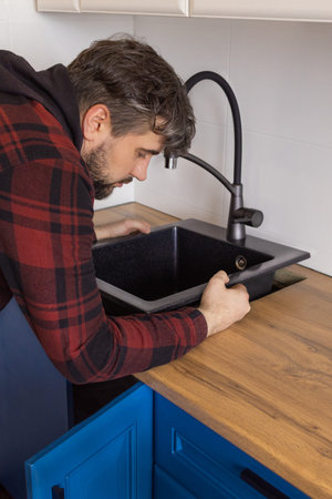 Man installing black stone sink into wooden countertop in kitchen. Vertical photoの写真素材