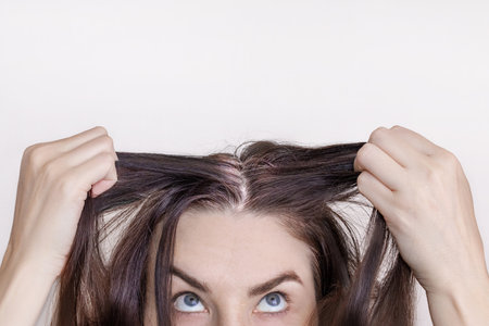 Caucasian brunette woman shows grown gray hair. Isolated on white background. Close up photoの写真素材