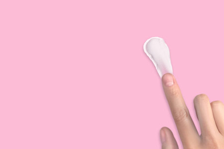 A woman's hand smears white cream. Swatch of white moisturizer. Cream texture, copy space pink...