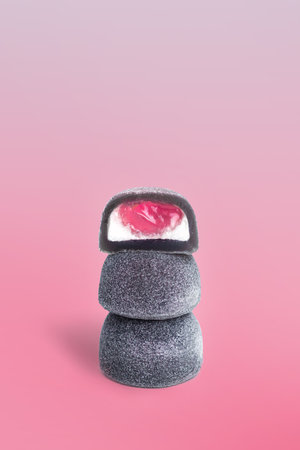 Mochi - Japanese dessert, sweets. From rice dough. A black Mochi with red berry filling Isolated on a pink Background vertical photoの写真素材
