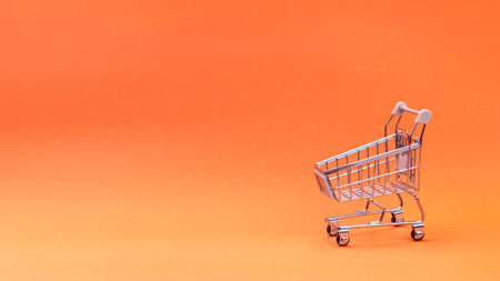 Supermarket concept. An empty supermarket trolley isolated on an orange background. Free space for your text, copy space bannerの写真素材