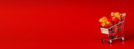 Supermarket trolley with red box with gold bows. The concept of buying gifts for holidays and sales. Discounts, Black Friday. Red background, Copy space long horizontal banner photoの写真素材