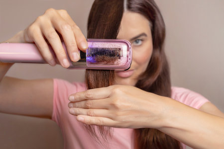 Woman looks after her hair. She uses a machine to cut the split ends of her hair. Split ends treatment with trimmer, hair self-careの写真素材