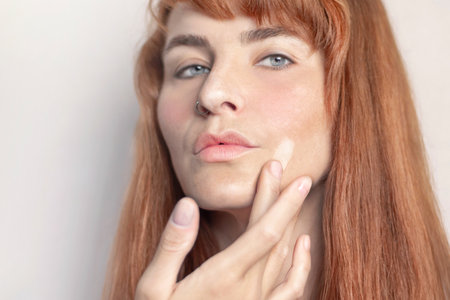 Red-haired caucasian girl puts foundation on her face with her fingerの写真素材