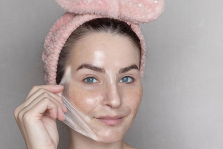 Caucasian woman makes a cosmetic Peel Off Mask. She removes the film mask with her hand Close up, copy spaceの写真素材