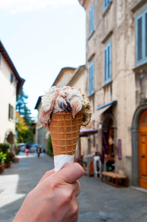 Hand holding gelato, ice-cream with blur background of a old town in Italyの写真素材