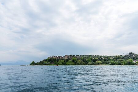 Sirmione, Italy - April 29, 2018: Amazing panoramic view of Grotte di Catullo from the Garda Lake. The ruins of a Roman villa and Stony Beach. Ancient Roman archaeological site in Sirmione.のeditorial素材